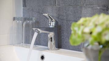 A bathroom with a modern faucet, a glass sink, and a potted plant.