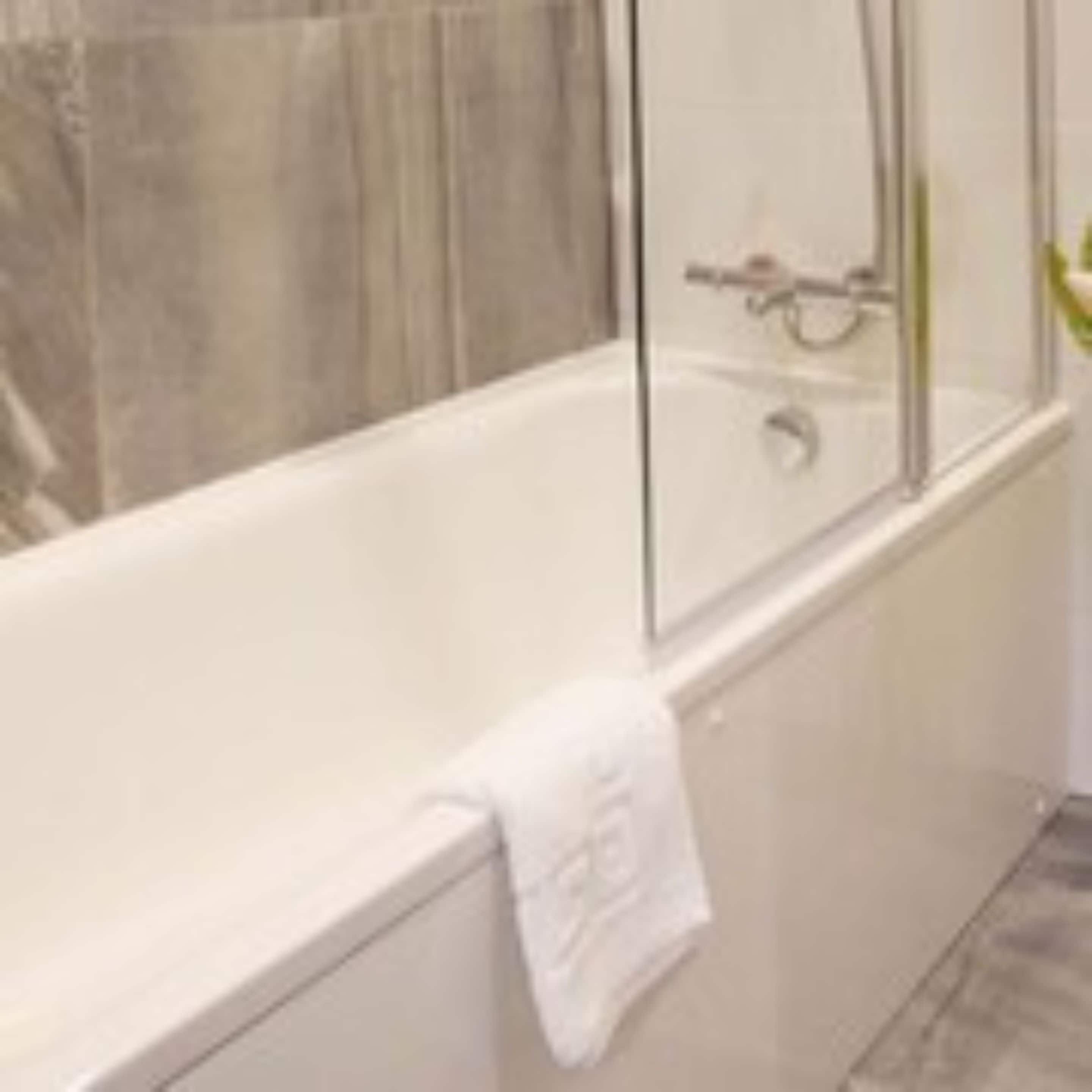 Un baño moderno con una bañera acristalada, zona de ducha a la vista y pared revestida de mármol.
