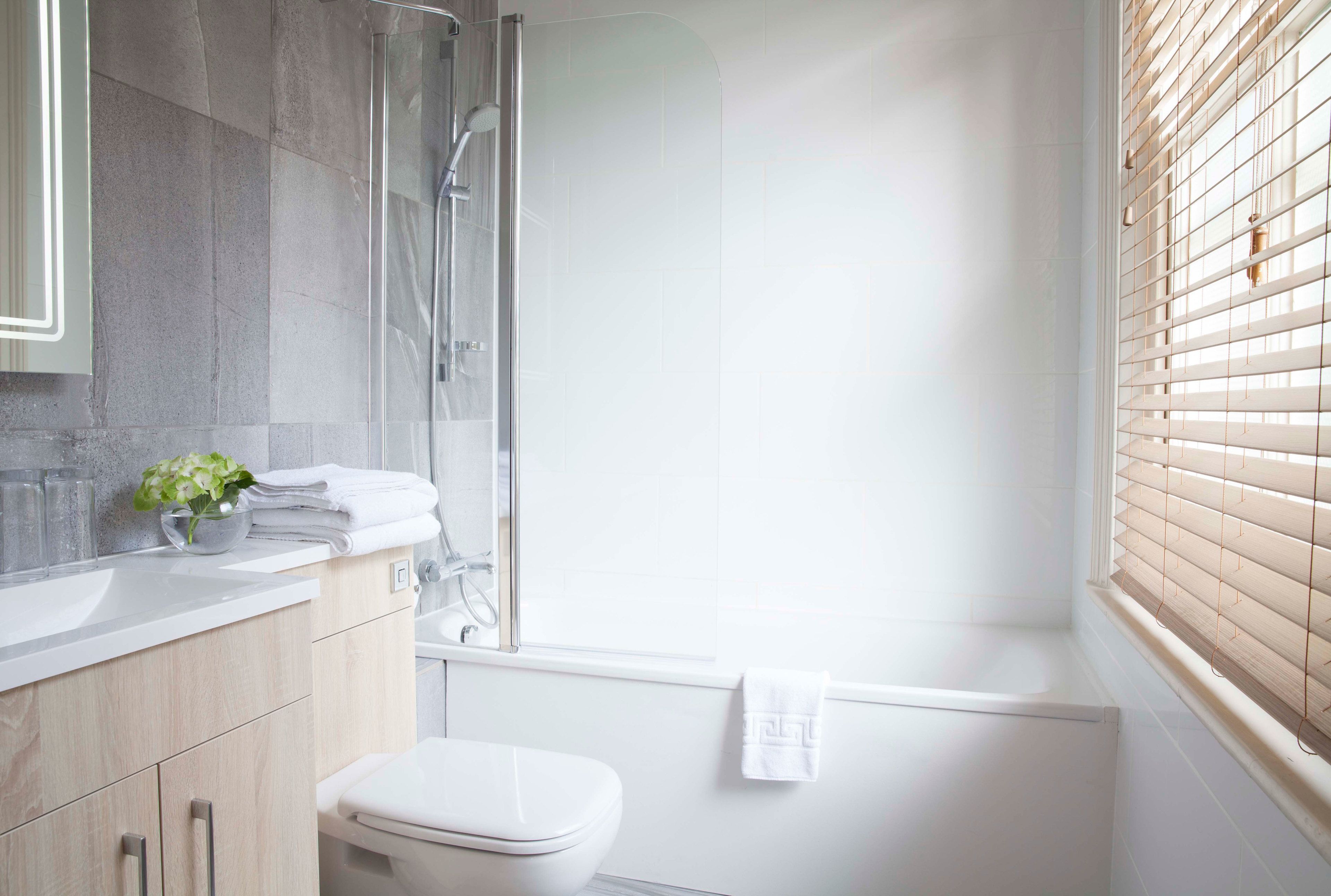 Un baño moderno con cabina de ducha de vidrio, inodoro blanco y lavamanos con una planta.