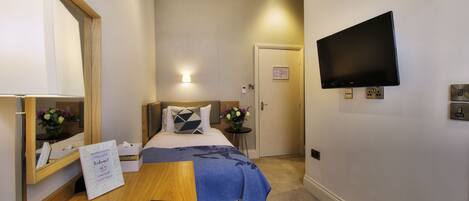 A hotel room with a bed, a desk, a telephone, a TV, and a mirror.