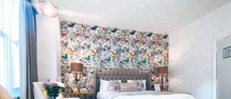 Un dormitorio con una cama, una silla, una mesita de noche y una pared con estampado floral.