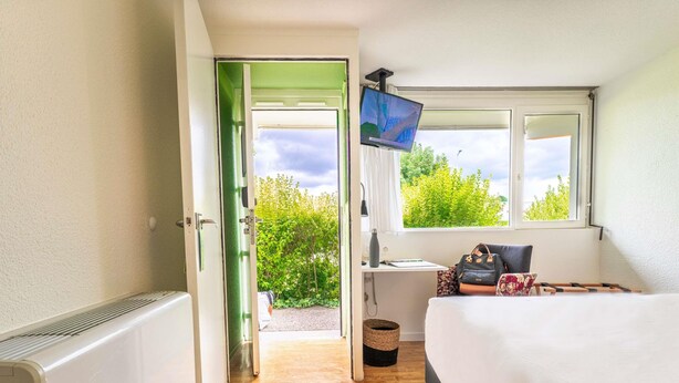 Une chambre à coucher avec un lit, un bureau, une télévision et une fenêtre donnant sur un paysage verdoyant.