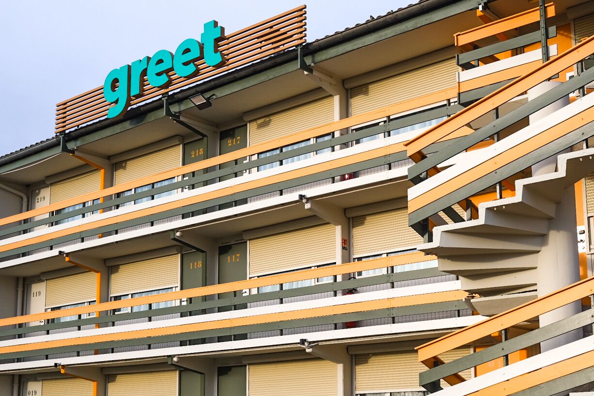 Ein mehrgeschossiges Gebäude mit einem gut sichtbaren, grünen Schild auf dem Dach.