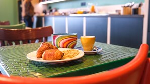 Une table verte dressée pour le petit-déjeuner, avec des croissants, un bol coloré et un verre de jus d’orange.