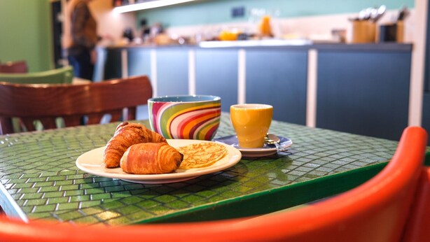 A breakfast setting with croissants, a colorful bowl, and a glass of orange juice on a green table.