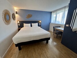 A bedroom with a bed, bedside lamps, a desk, and a chair.