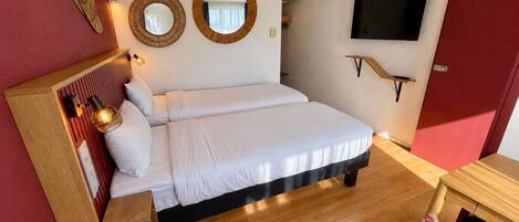 Habitación de hotel con cama, lámpara de noche, espejos en la pared, televisor y mesita de noche de madera.