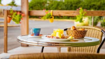 Une table ronde en verre, sur laquelle sont disposés des aliments pour le petit-déjeuner, notamment une tasse bleue, un panier de pain et une assiette avec des œufs et des toasts.