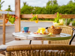 A round glass table with breakfast items including a blue cup, a basket of bread, and a plate with eggs and toast.