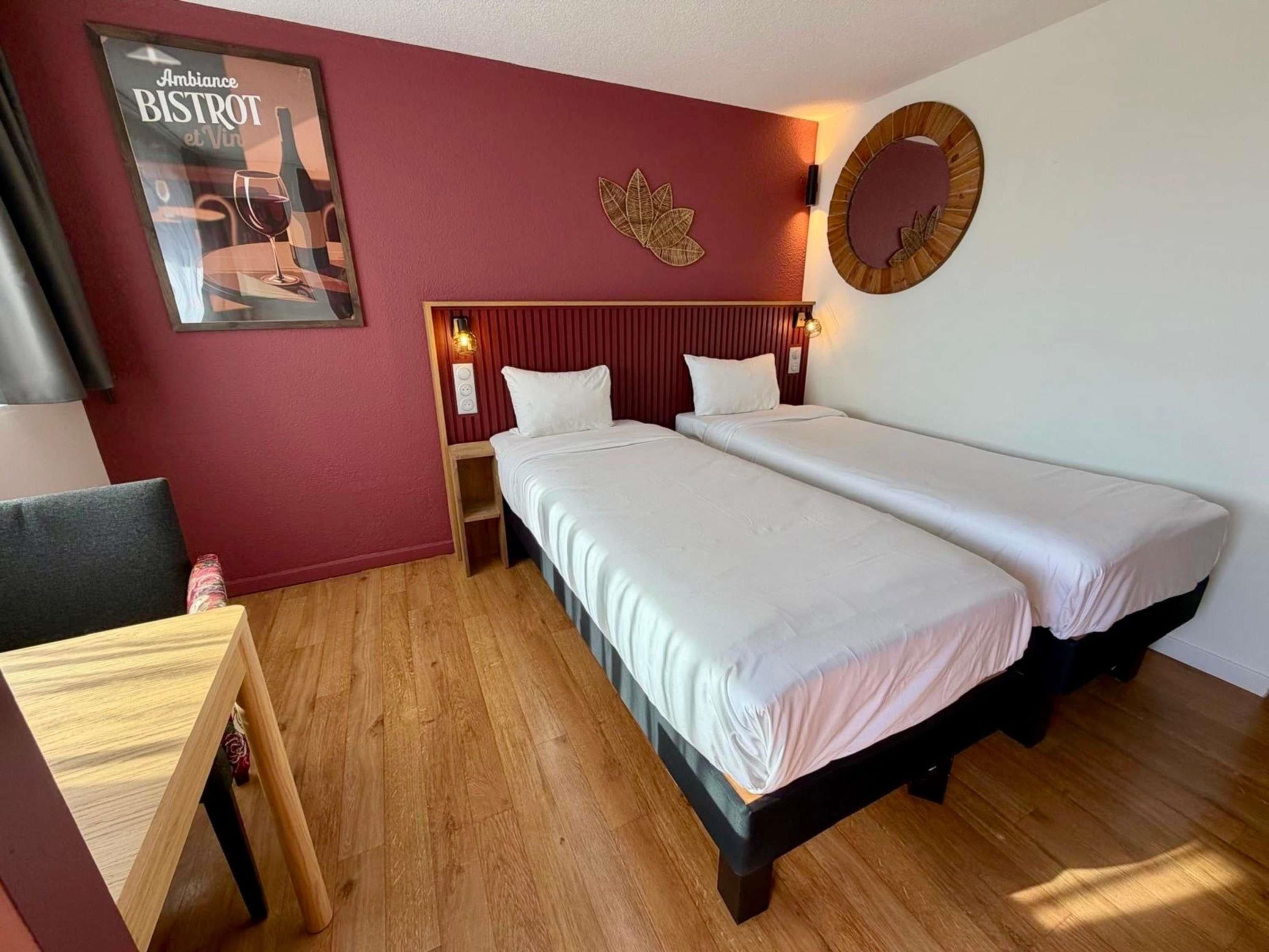 Ein Hotelzimmer mit zwei Betten, einem Holztisch, einem Poster an der Wand und einer Wandleuchte.