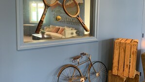 Une pièce avec un grand miroir dans lequel se reflètent des raquettes de tennis et un vélo, une caisse en bois et un mur bleu.
