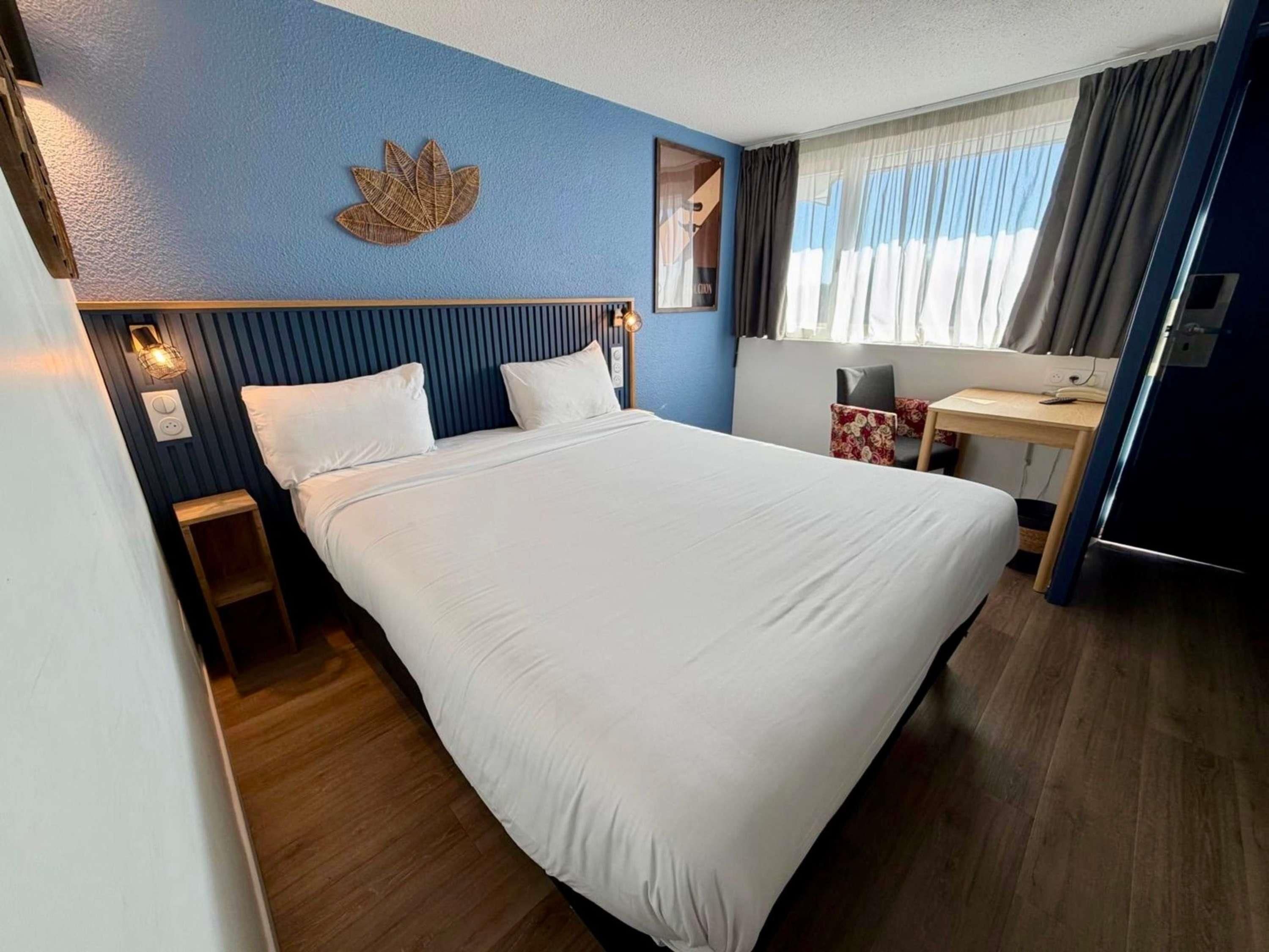 A hotel room with a bed, bedside tables, a desk, and a window with curtains.