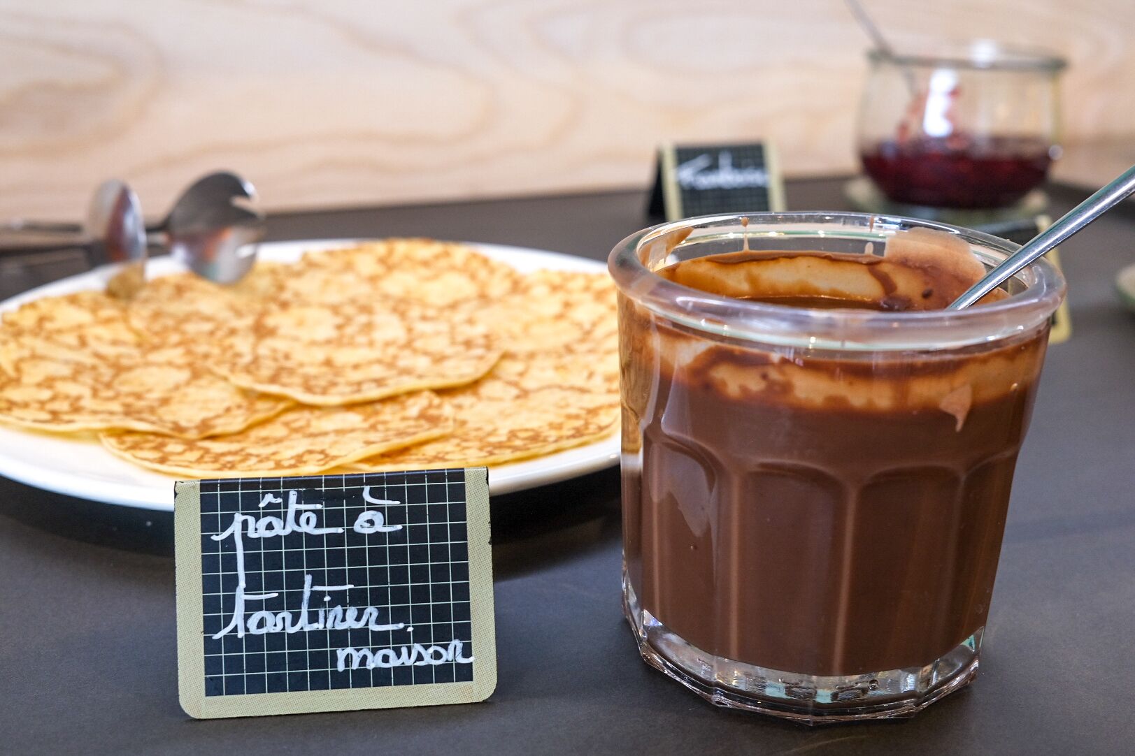 Ein Glas Eiskaffee mit einem Löffel, ein Teller mit Crepes und ein Kreidetafel mit Schrift.