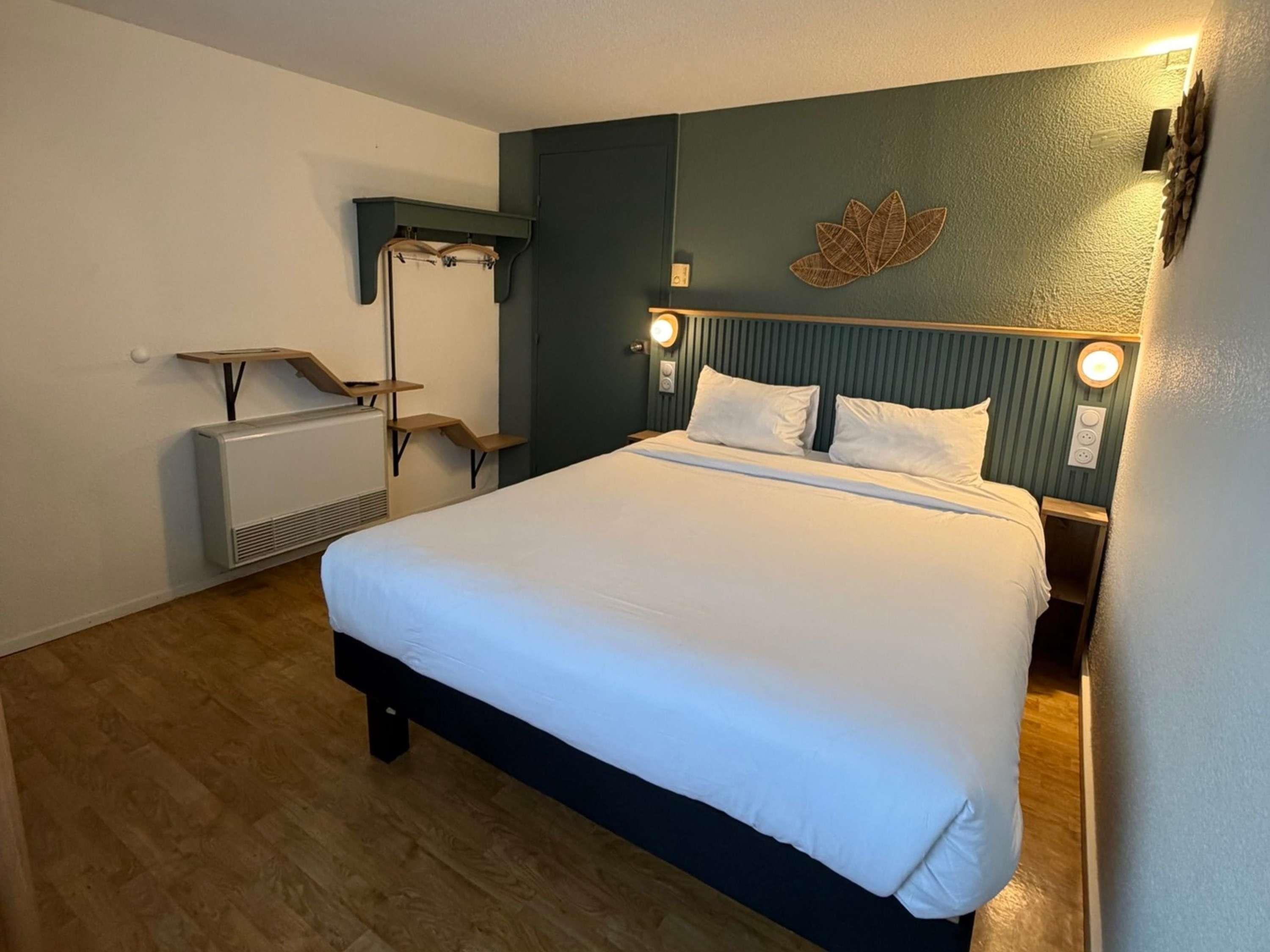 A hotel room with a bed, bedside table, lamp, and a wall-mounted decorative element.