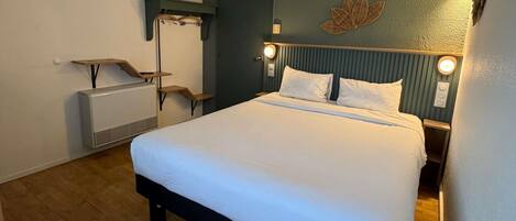 A hotel room with a bed, bedside table, lamp, and a wall-mounted decorative element.