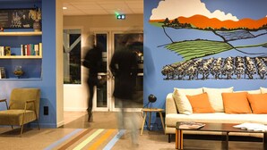 A modern lobby with a blue wall, a bookshelf, a sofa with orange cushions, and a coffee table.