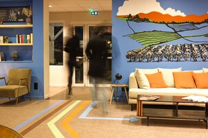 A modern lobby with a blue wall, a bookshelf, a sofa with orange cushions, and a coffee table.