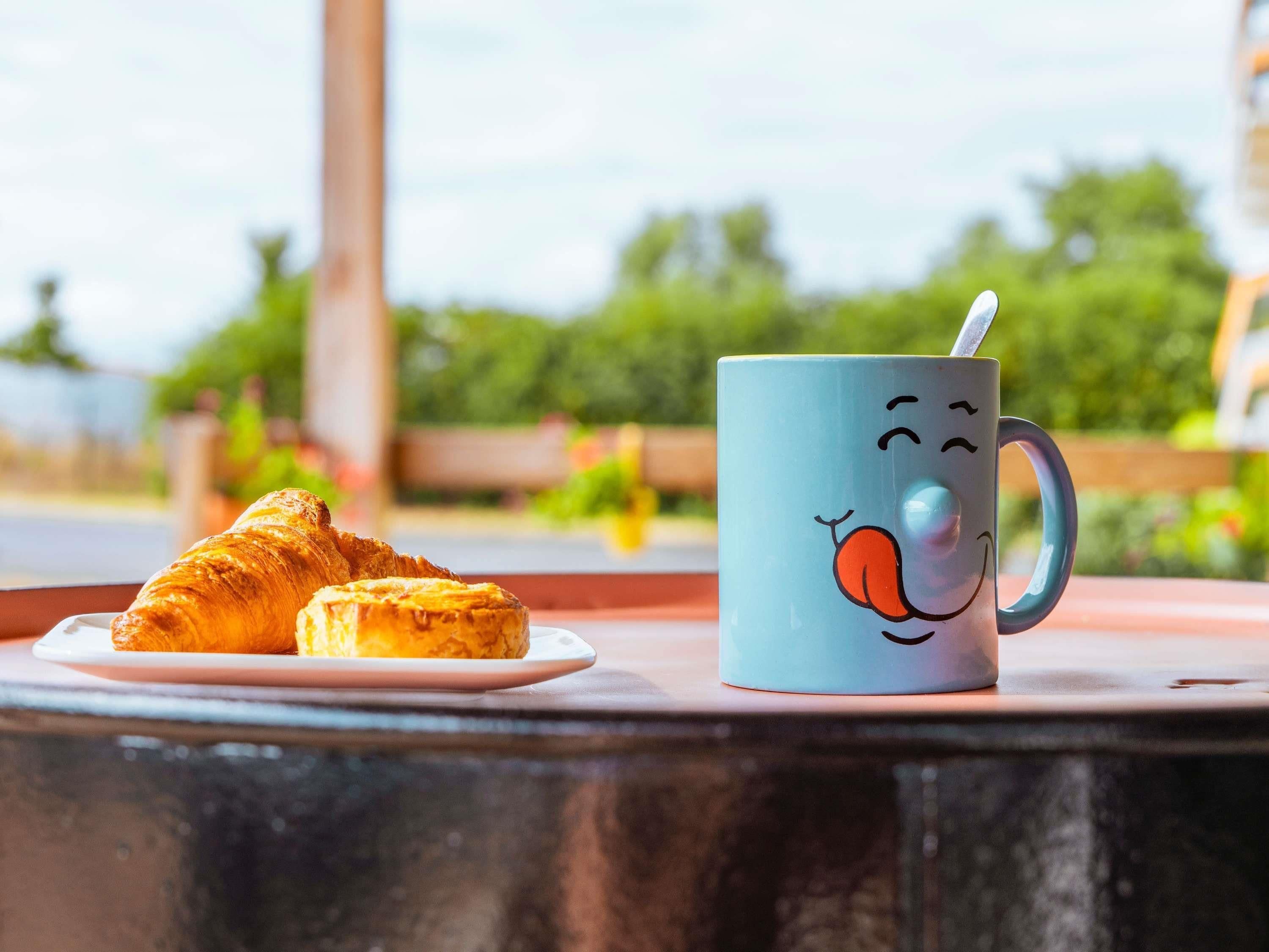 Una mesa con un plato de cruasanes y una taza con una carita sonriente.