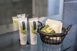 Two tubes of Virgin Olive Oil hair and body wash on a glass surface, with a wicker basket containing additional items.