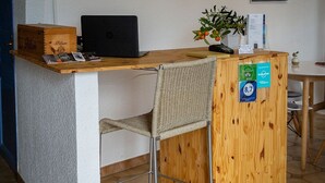 A reception desk with a laptop, a plant, and a wooden cabinet. There is a calendar on the wall and a poster above the desk. - Hôtel Du Soleil (Saint-Raphael)
