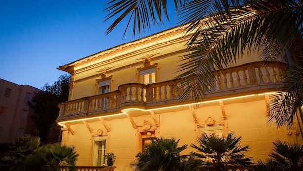 A multi-story building with a balcony, palm trees, and warm lighting. - Hôtel Du Soleil (Saint-Raphael)