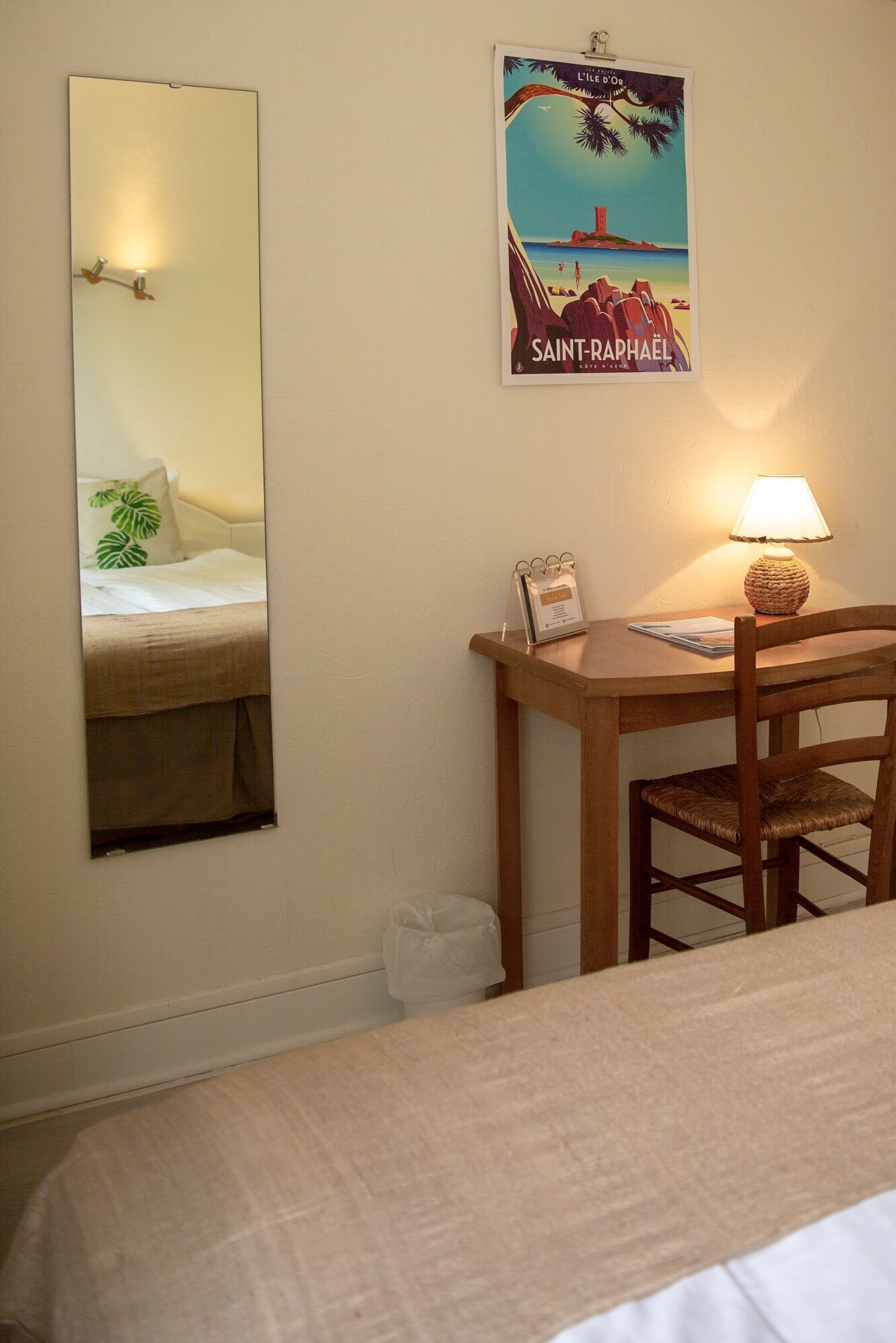 Une chambre d’hôtel avec un lit, un bureau et une chaise, une lampe, une affiche au mur et un miroir.