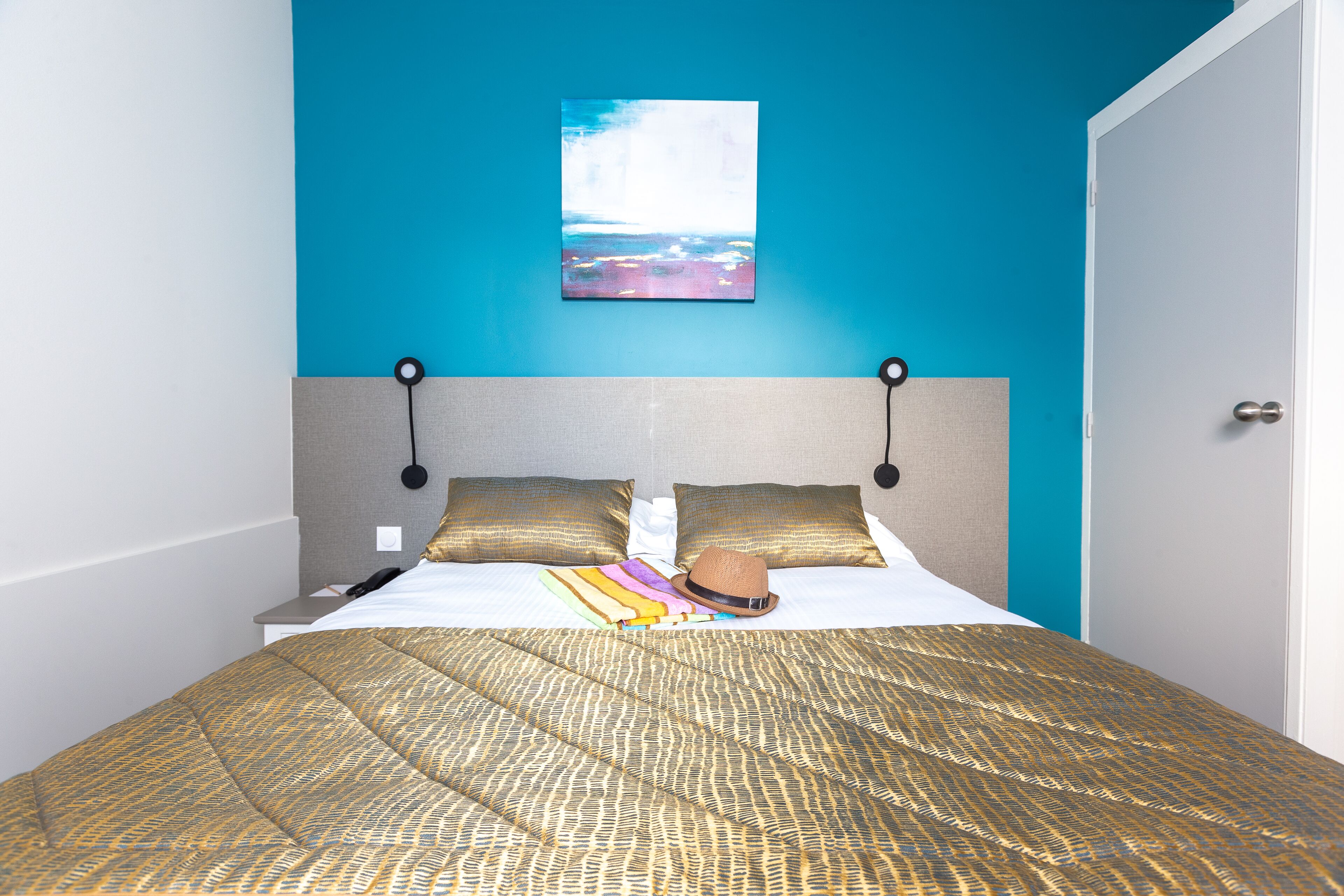 A neatly made bed with a patterned bedspread, two pillows, and a hat on the bed.