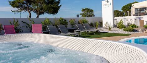 A hot tub area with lounge chairs, a pool, and a building with a sign.
