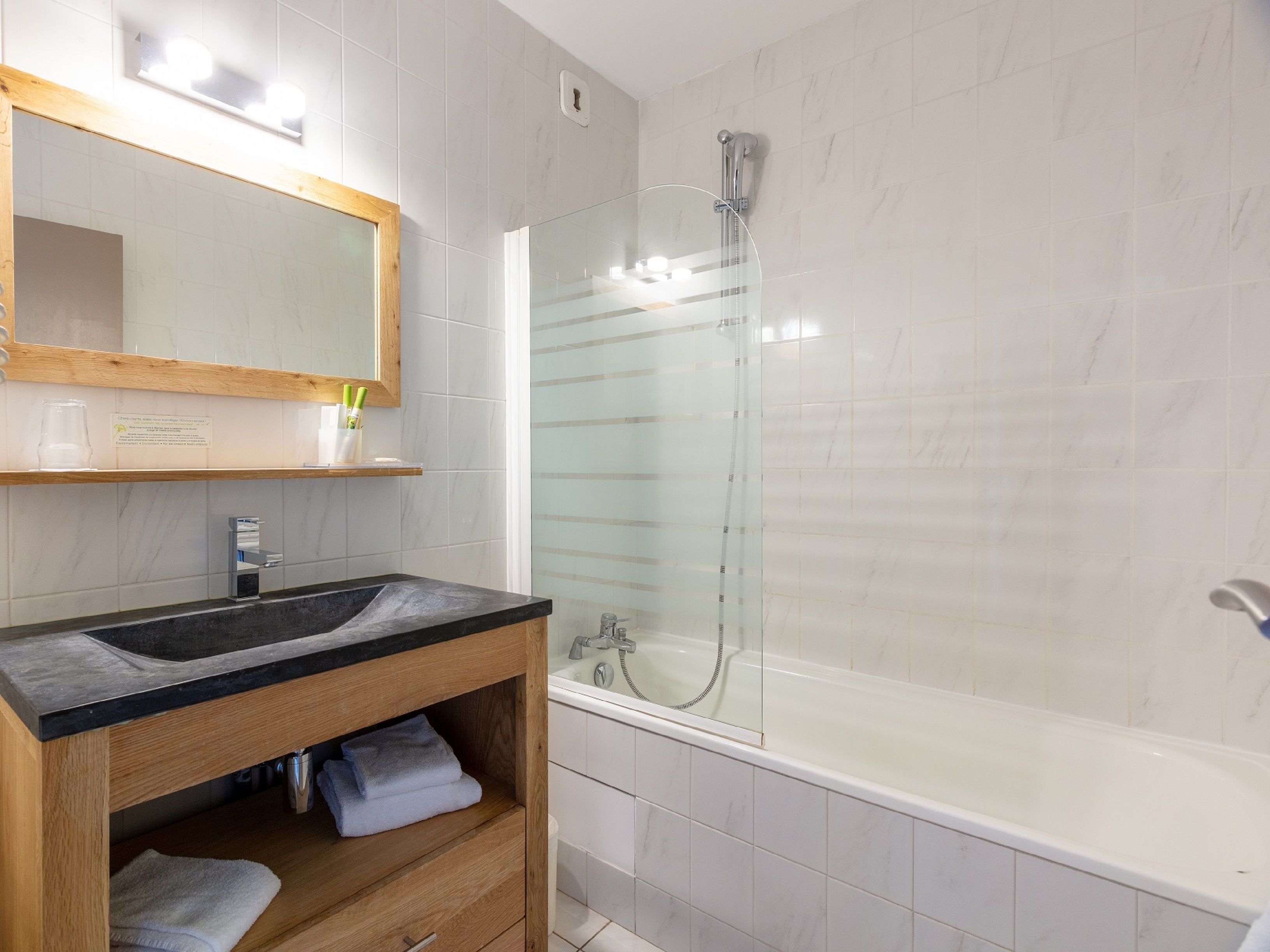 Un bagno moderno con un mobile bagno in legno, cabina doccia in vetro e vasca da bagno bianca.