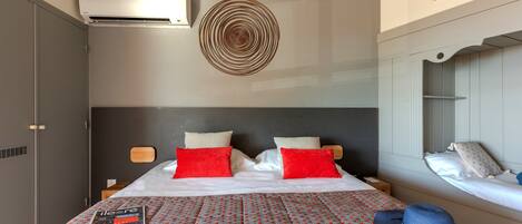 A hotel room with a bed, two pillows, a magazine, a hat, and a wall art piece.