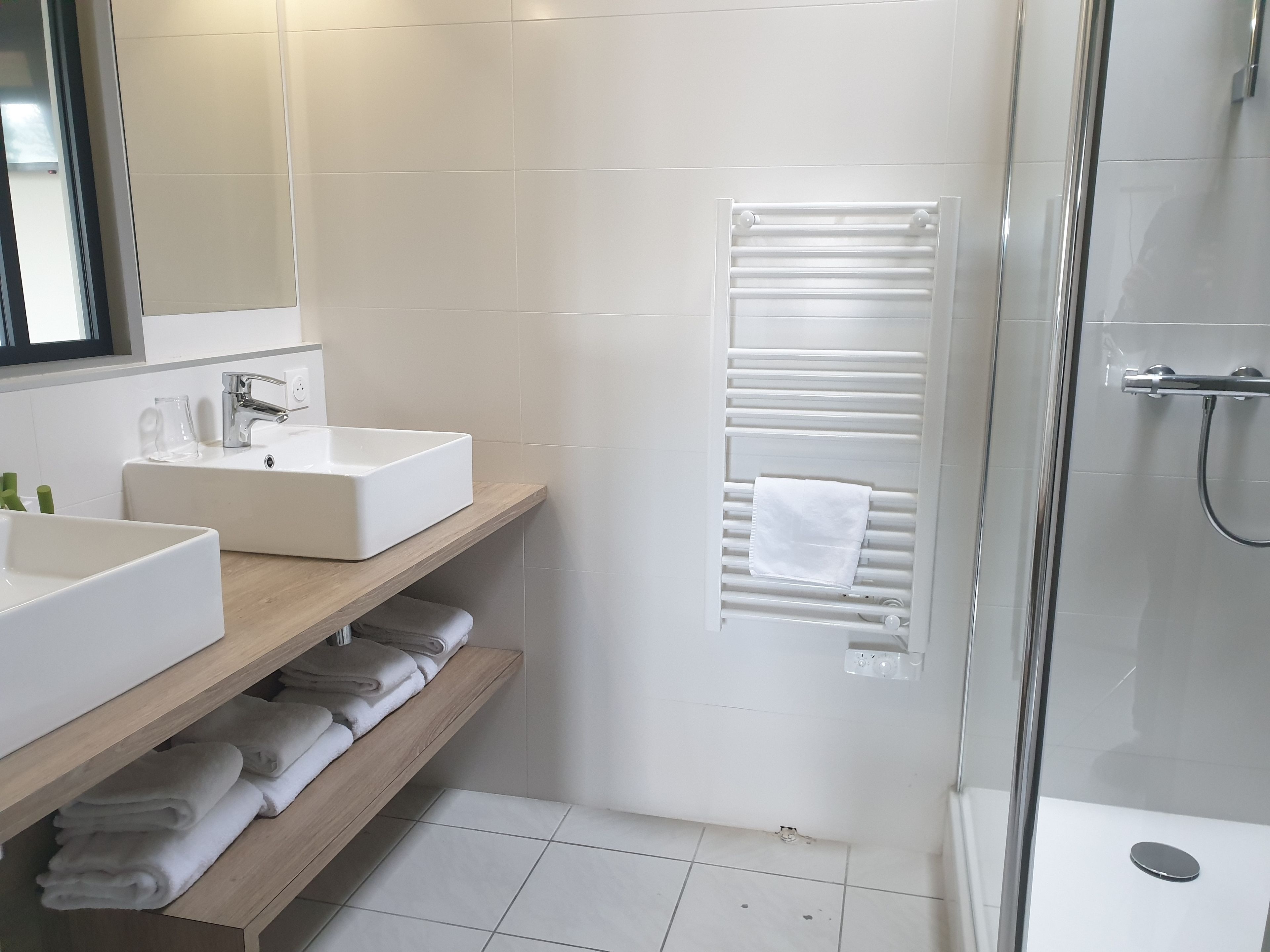 A modern bathroom with two sinks, a mirror, a towel rack, and a glass shower enclosure.