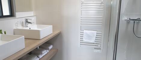 A modern bathroom with two sinks, a mirror, a towel rack, and a glass shower enclosure.