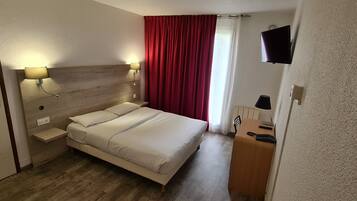 Habitación de hotel con cama, lámparas de noche, televisión, escritorio y cortina roja.