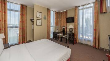 A hotel room with a large bed, a desk with a chair, a TV mounted on the wall, and curtains with a floral pattern.