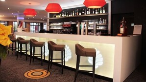 Una zona de bar con mostrador, taburetes y estanterías llenas de botellas.