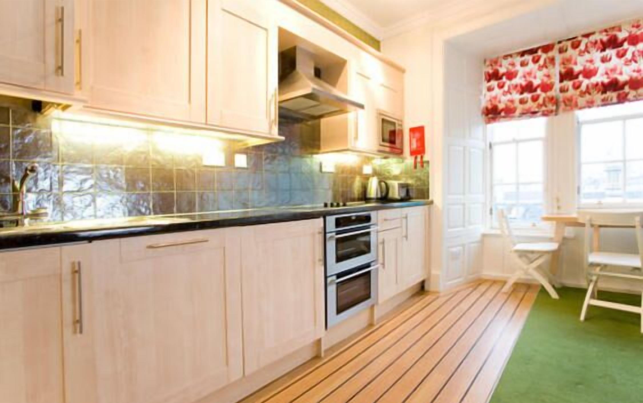 A kitchen with light-colored cabinets, a stainless steel oven, and a window with a floral curtain.