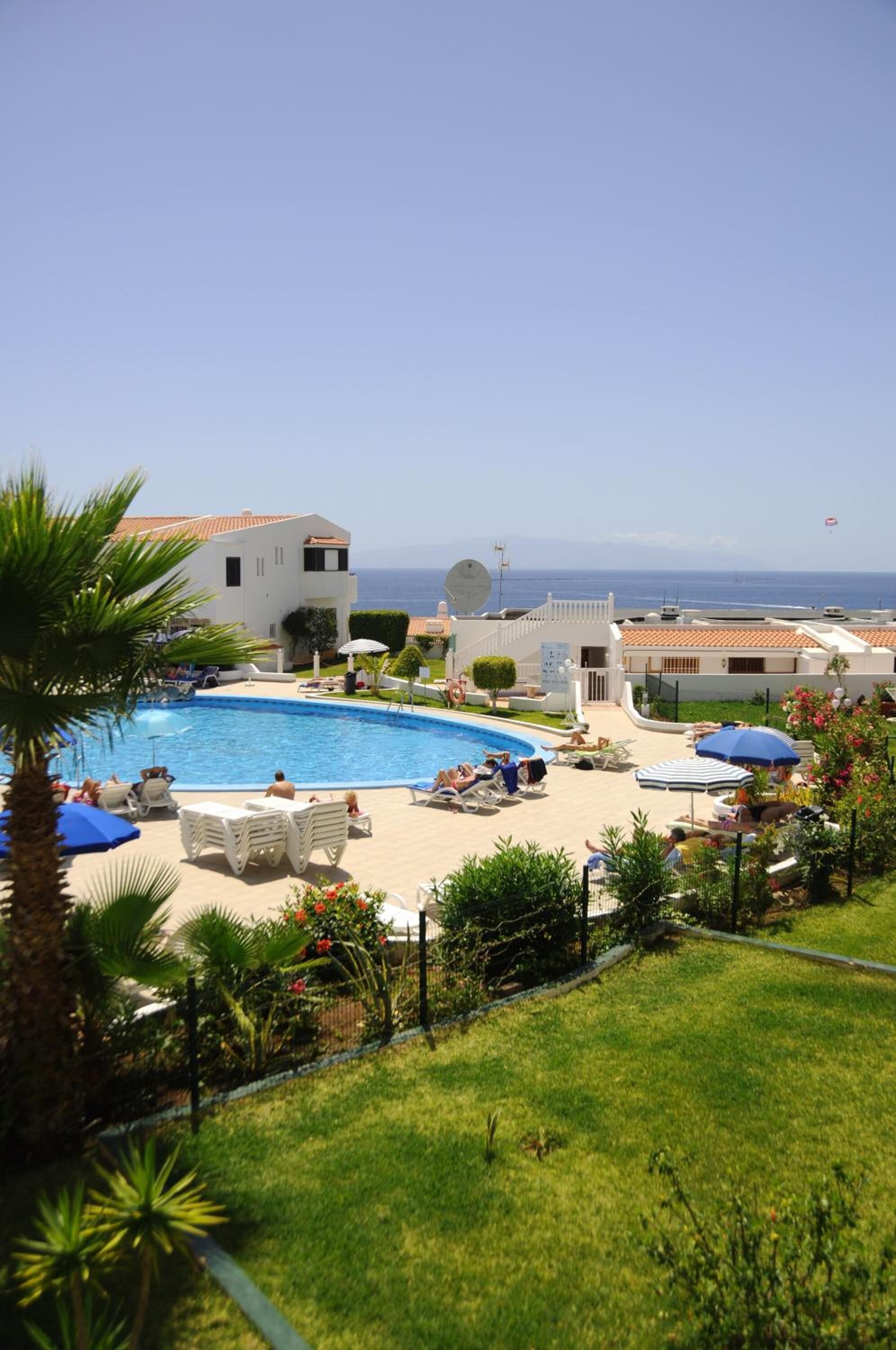A pool area with lounge chairs and umbrellas, surrounded by greenery and a view of the sea.