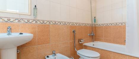 Een badkamer met een wastafel, toilet, bad en bidet.