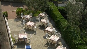 An outdoor seating area with tables and chairs, surrounded by greenery and a paved walkway. - Delle Rose (Torri del Benaco)