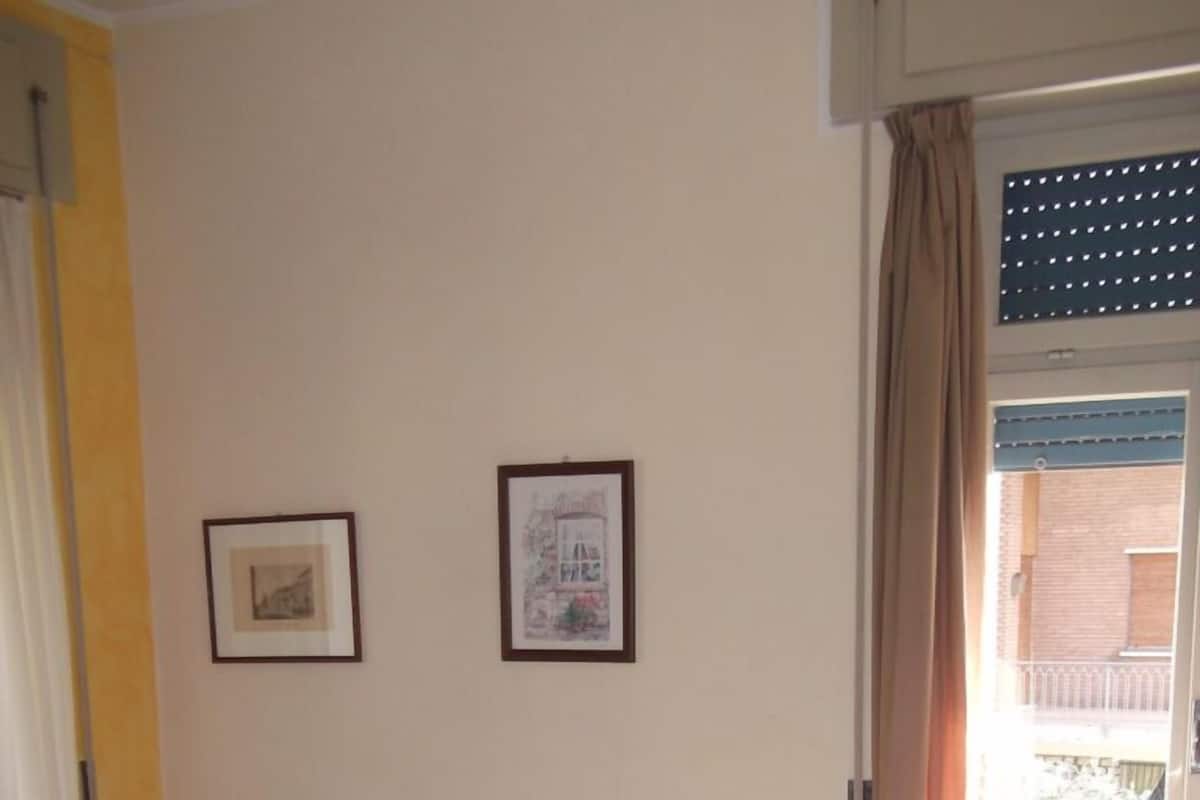 A room with two beds, a chair, and two framed pictures on the wall.