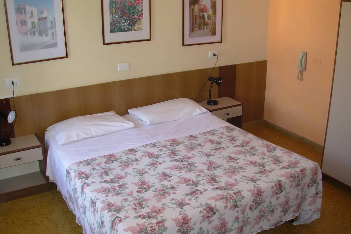 A neatly made bed with a floral bedspread, two bedside tables with lamps, and three framed pictures on the wall.