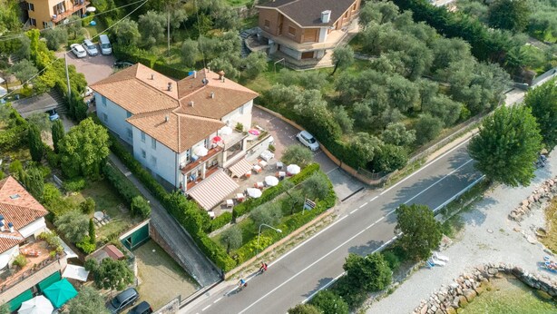 An aerial view of a residential area with a large house featuring a tiled roof, a swimming pool, and a well-maintained garden. - Delle Rose (Torri del Benaco)
