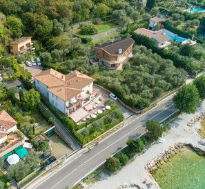 An aerial view of a residential area with a large house featuring a tiled roof, a swimming pool, and a well-maintained garden. - Delle Rose (Torri del Benaco)