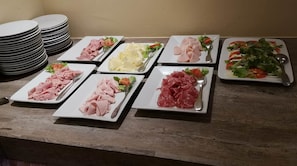 A wooden table with multiple white plates of various food items, including sliced meats and salads. - Delle Rose (Torri del Benaco)