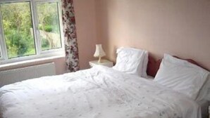 A bedroom with a bed, a window with curtains, a bedside table with a lamp, and a radiator. - Alpha Milton Guest House (Cambridge)