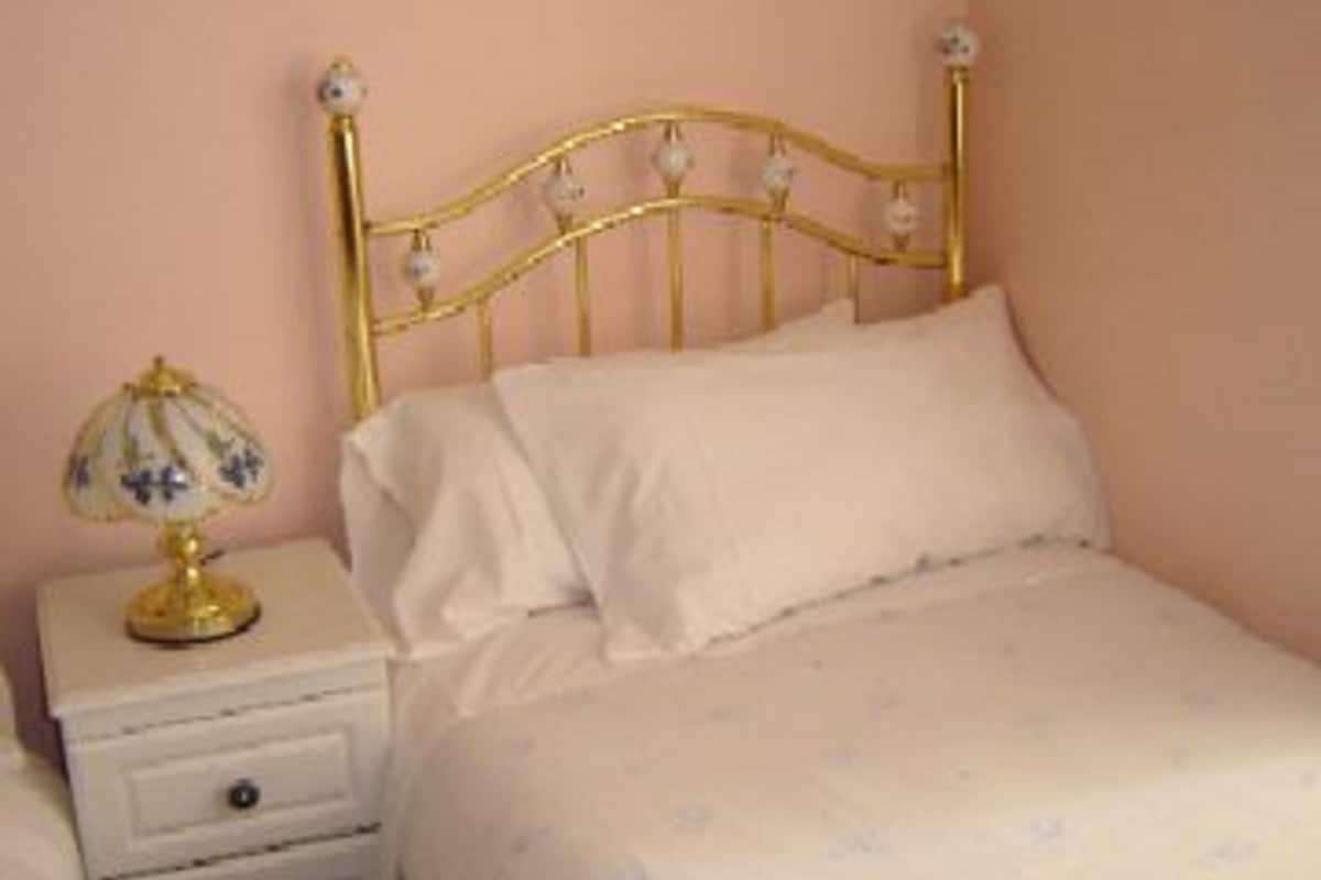 A bedroom with a gold metal bed frame, white bedding, and a bedside table with a lamp.