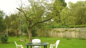 A grassy outdoor area with a table and two chairs, surrounded by trees and a wooden fence. - Alpha Milton Guest House (Cambridge)