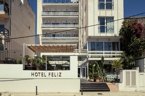 Hotellin sisäänkäynti, jossa on kyltti, jossa lukee ”HOTEL FELIZ”, katettu ulkoalue istumapaikkoineen ja ruukuissa olevia kasveja.