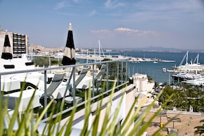 Un immeuble de grande hauteur doté d’une terrasse offrant une vue sur un port de plaisance où sont amarrés des bateaux et des yachts.