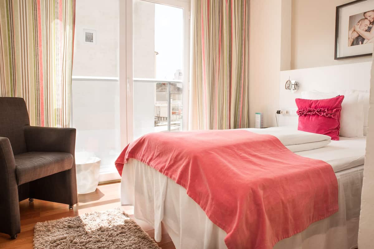 Un dormitorio con cama, una silla, una mesita de noche y vistas al balcón exterior.